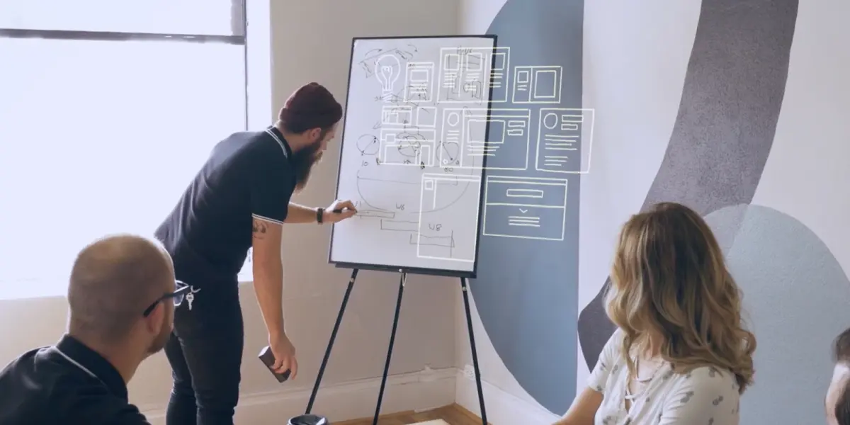 A group of Hounder employees collaborates around a whiteboard with wireframe sketches during a creative planning session.