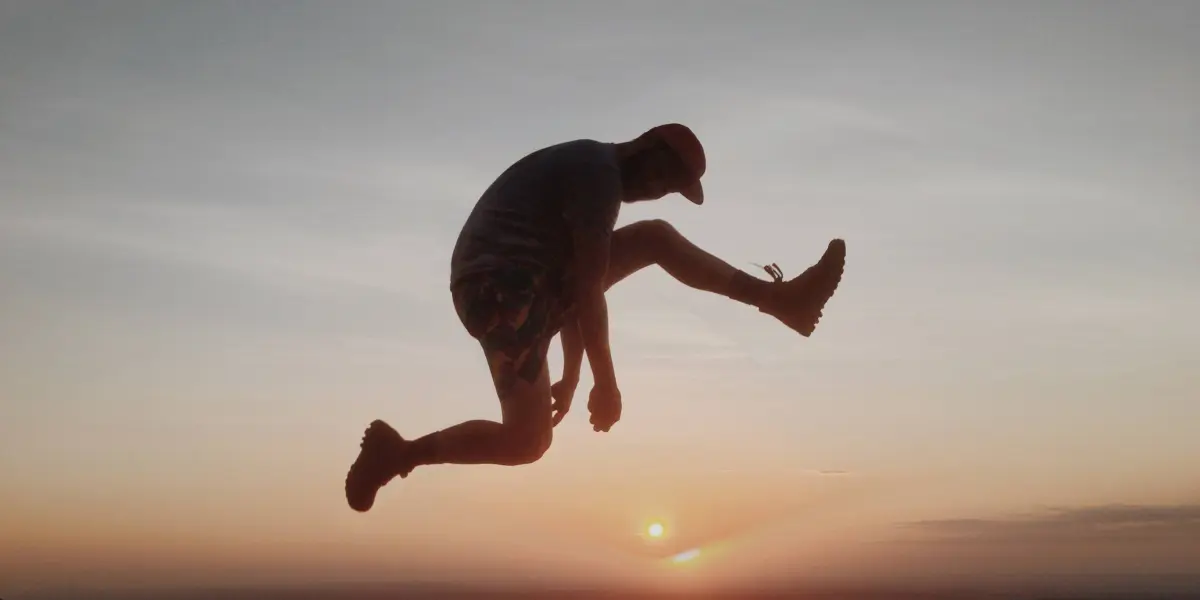 A man jumps mid-air in front of a vibrant sunset sky, silhouetted against the horizon.