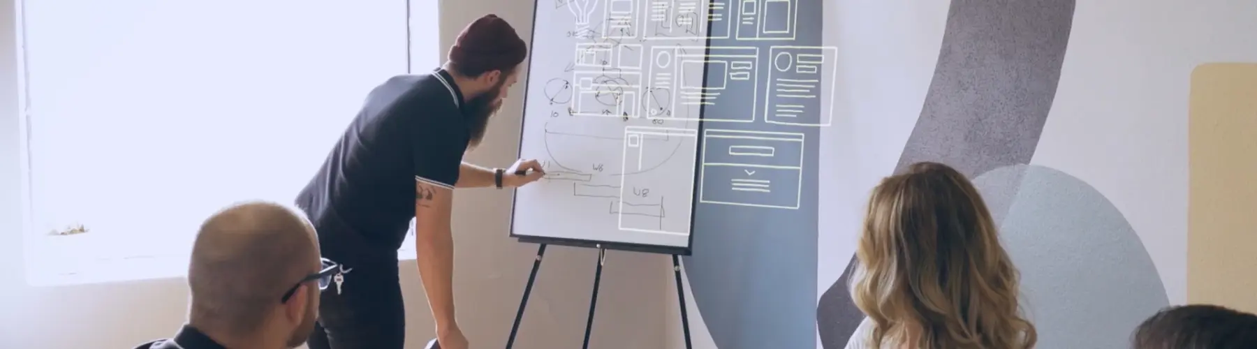 A group of Hounder employees collaborates around a whiteboard with wireframe sketches during a creative planning session.