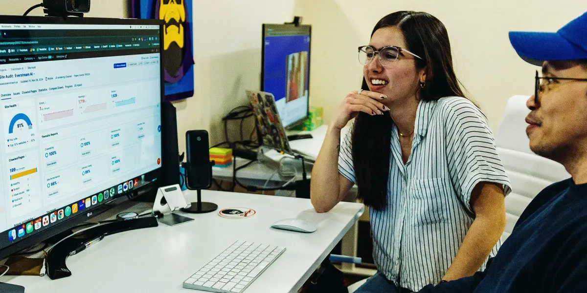 Two Hounder team members sit at a desk smiling while reviewing data on a computer screen.