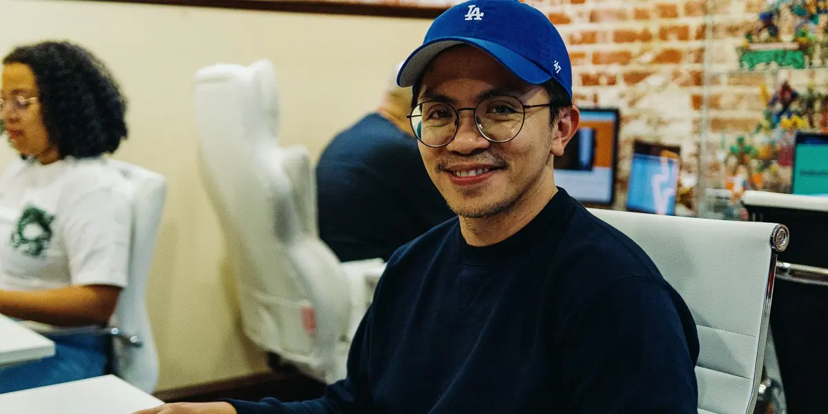 A Hounder team member wearing a blue LA cap smiles at the camera while working at a desk.