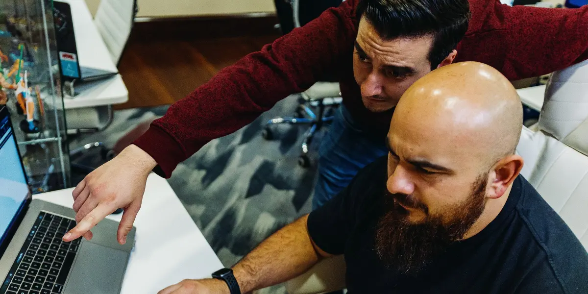 A Hounder employee points at a laptop screen while collaborating closely with a focused teammate.