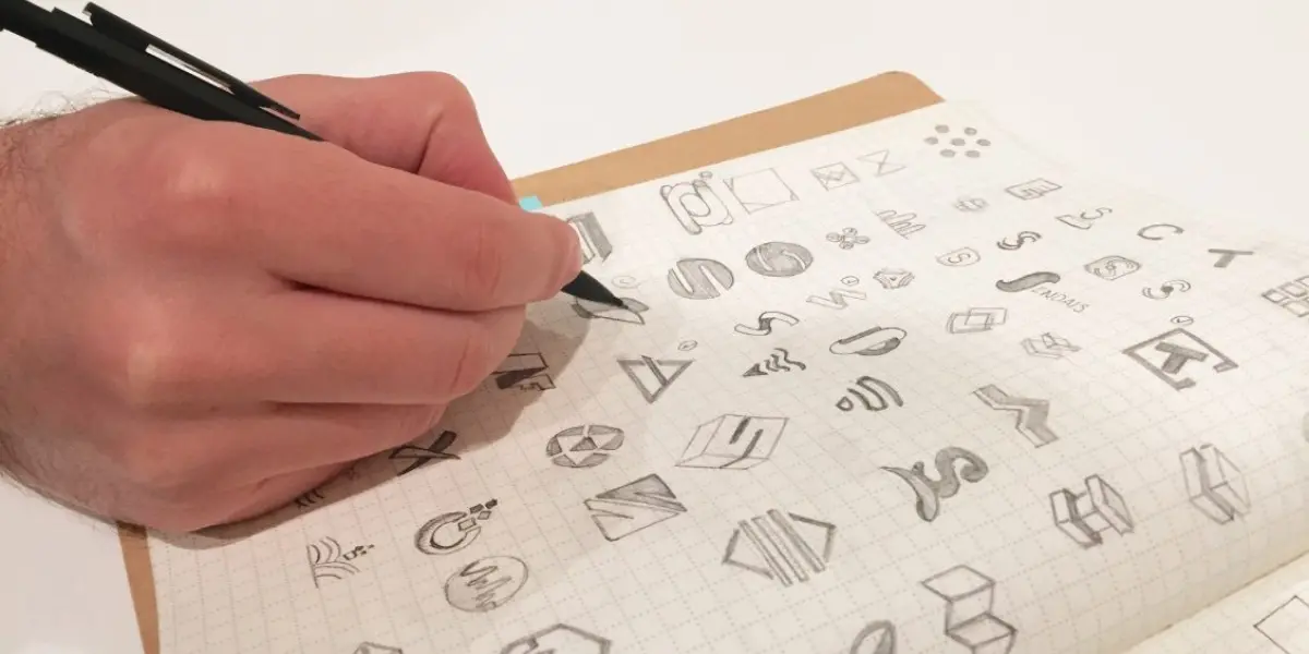 Hand sketching various logo concepts in a grid-lined notebook.
