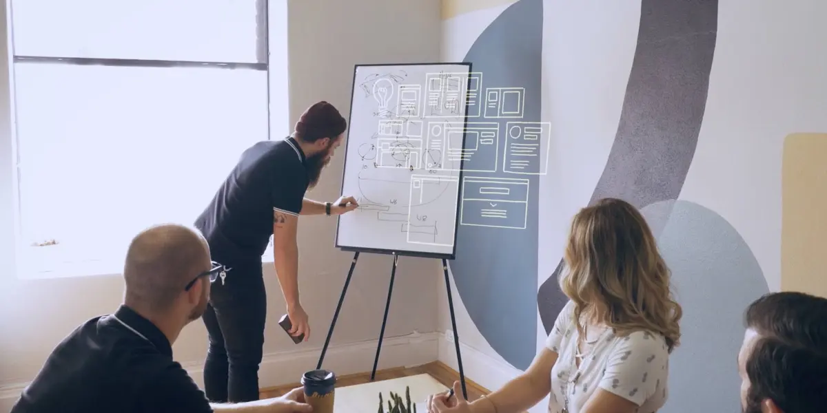 A group of Hounder employees collaborates around a whiteboard with wireframe sketches during a creative planning session.