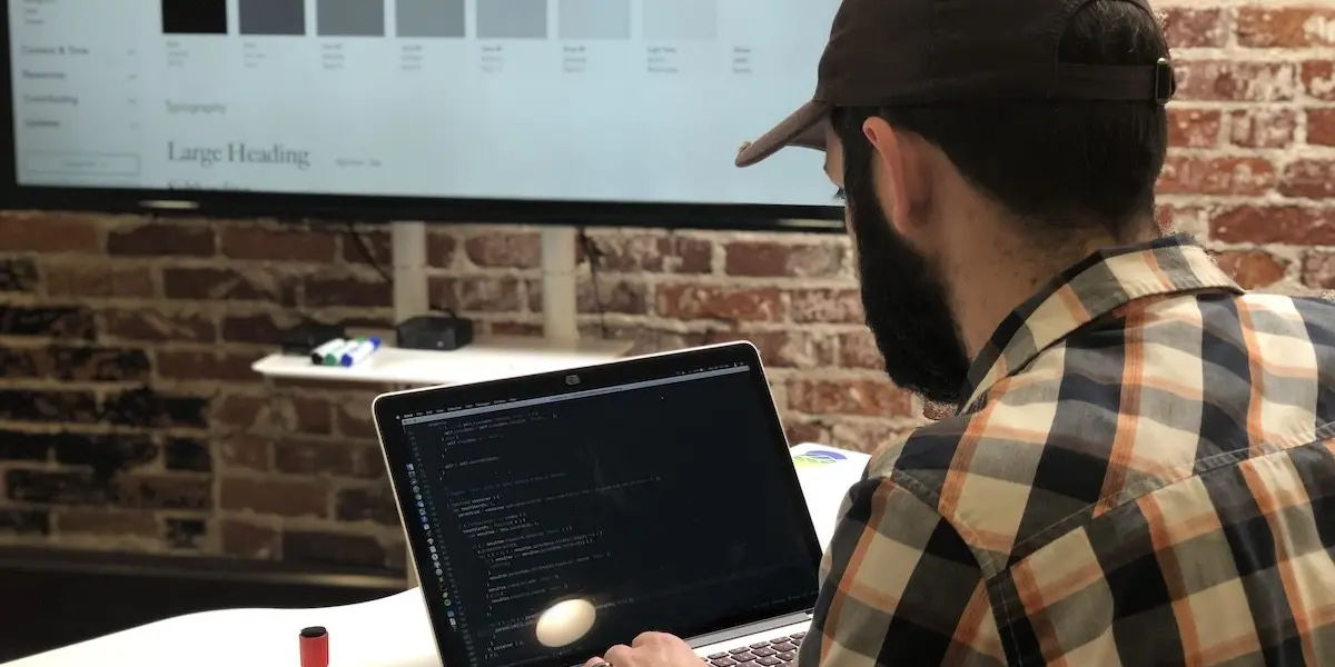 A Hounder developer codes on a laptop while referencing a large digital style guide displayed on a screen in front.