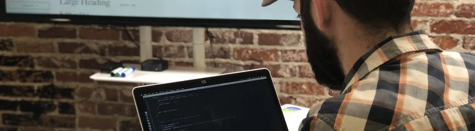 A Hounder developer codes on a laptop while referencing a large digital style guide displayed on a screen in front.