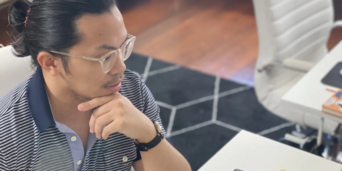 Person sits at a desk in a modern office space, thoughtfully looking at a computer screen just out of frame.