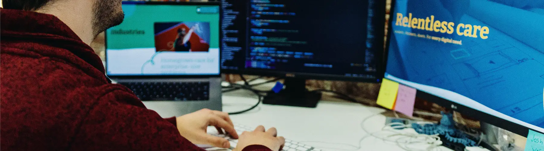 Person working at a desk with two monitors displaying code and graphics.