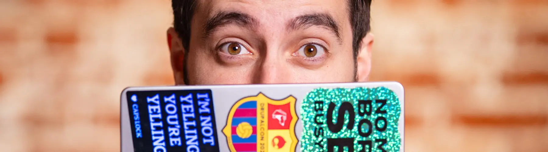 Man peeking over a laptop with colorful stickers.