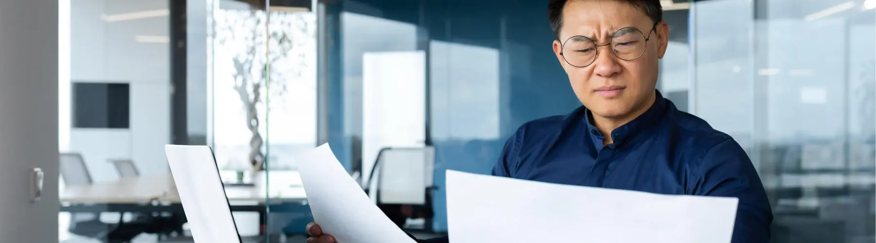 Man in a blue shirt reads papers in a modern office.