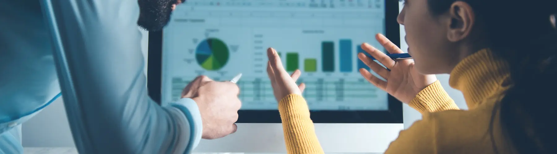 Two people discuss charts on a computer screen.