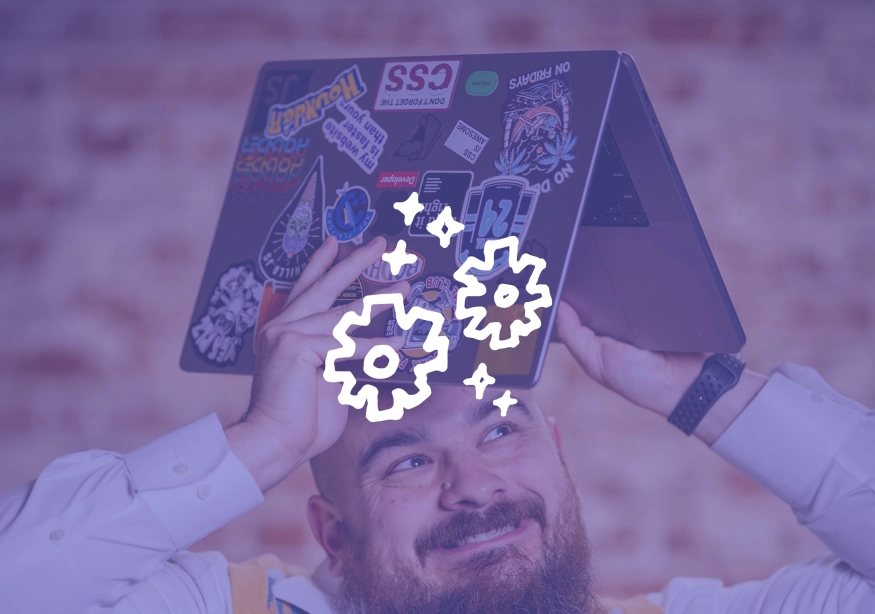 Man joyfully holds a sticker-covered laptop over his head with gear icons.