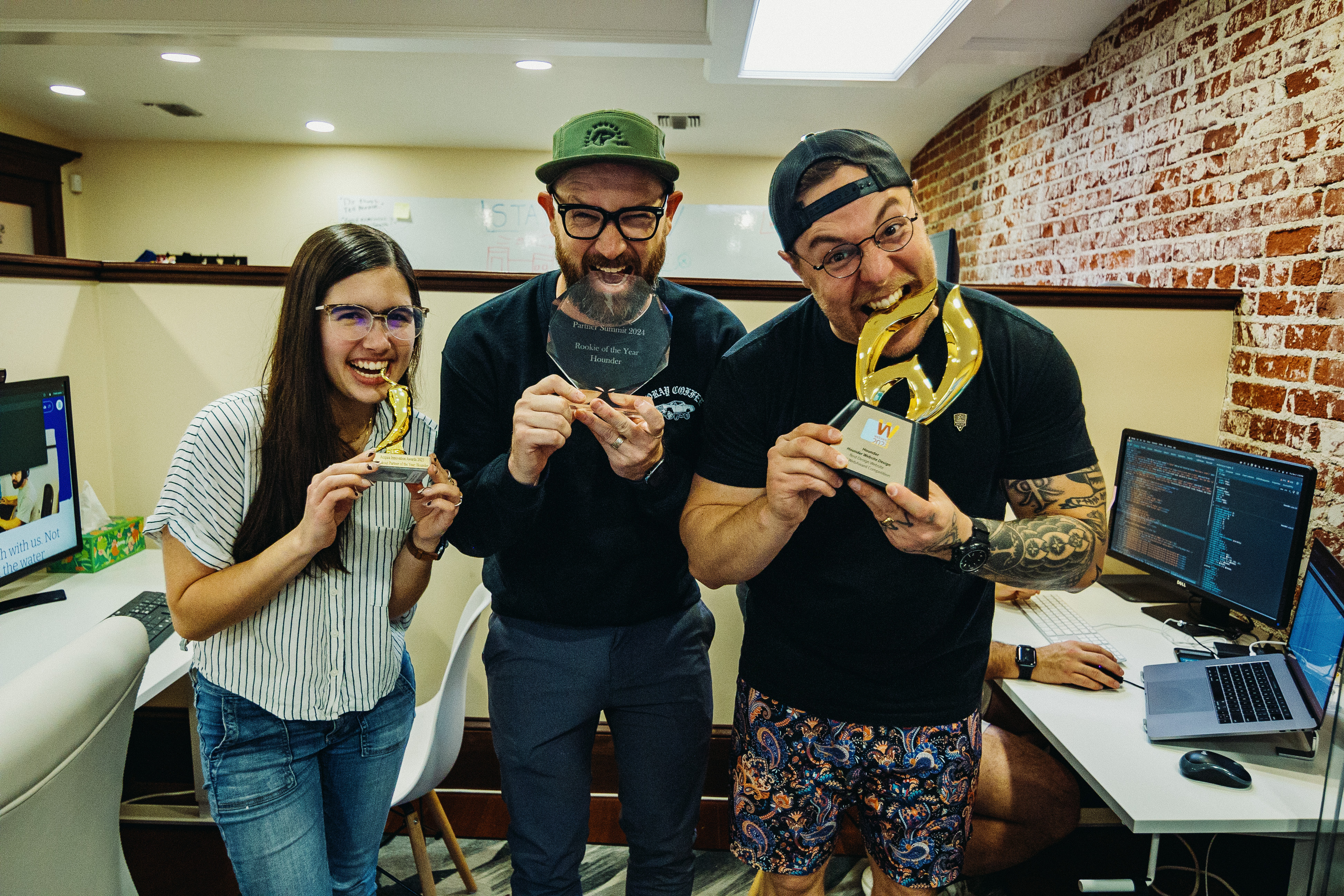 Three people smiling with awards in an office setting.