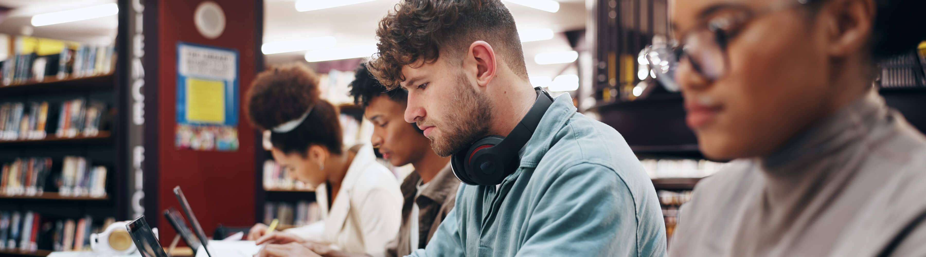 Students studying at a library table with laptops and books.