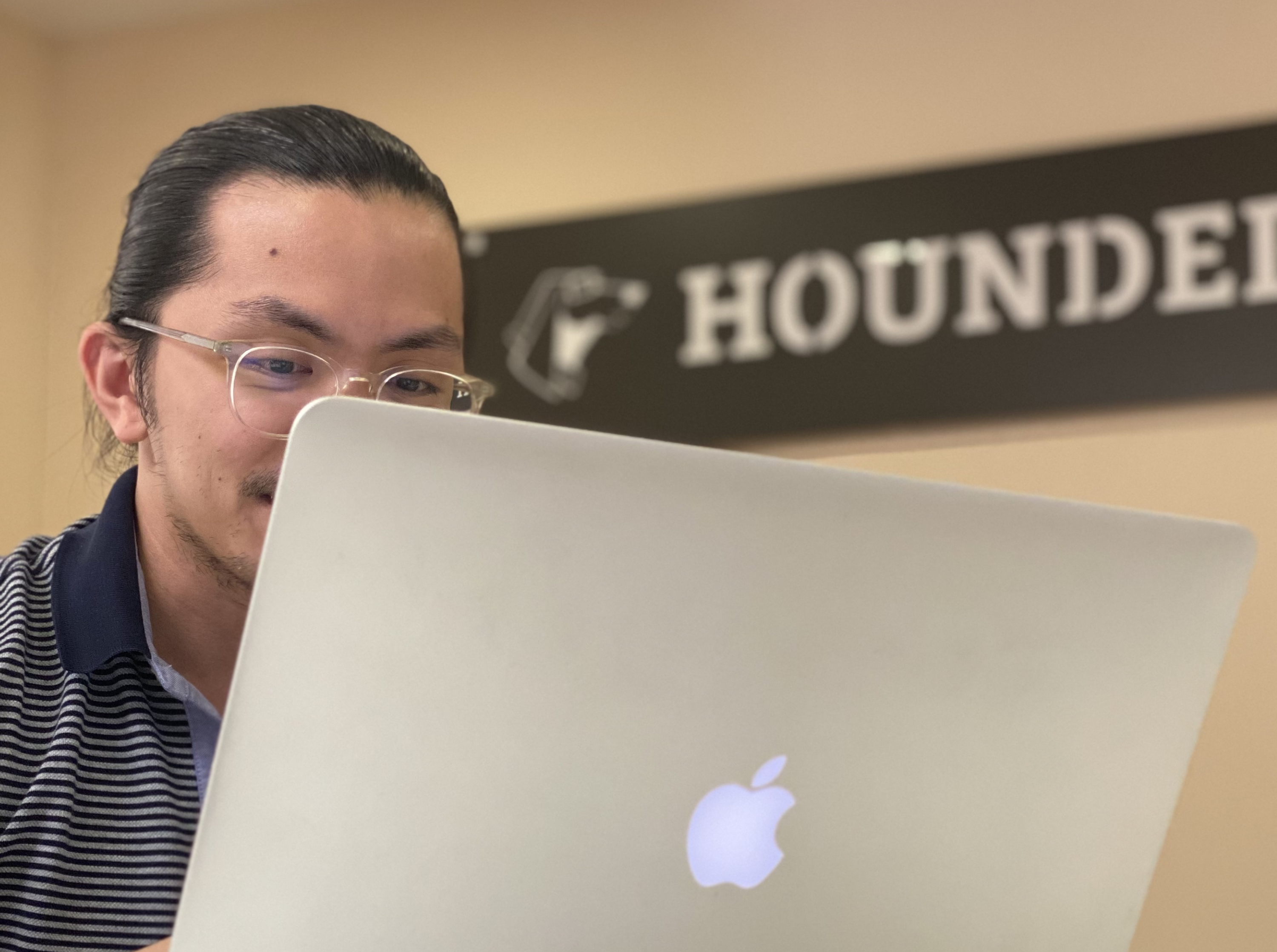 Man with glasses using a laptop, "HOUNDER" sign in the background.