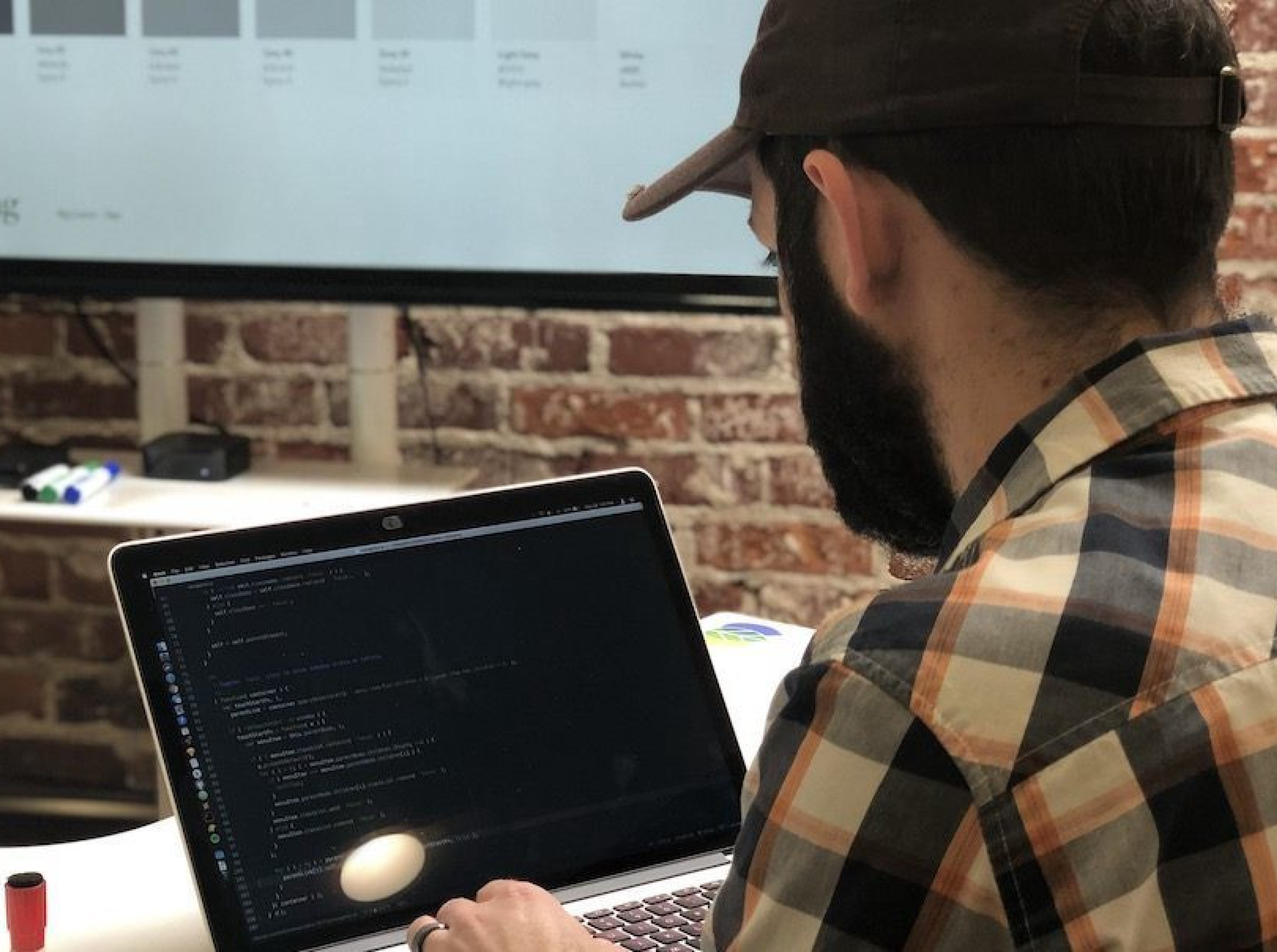 Man coding on a laptop in a brick-walled office.