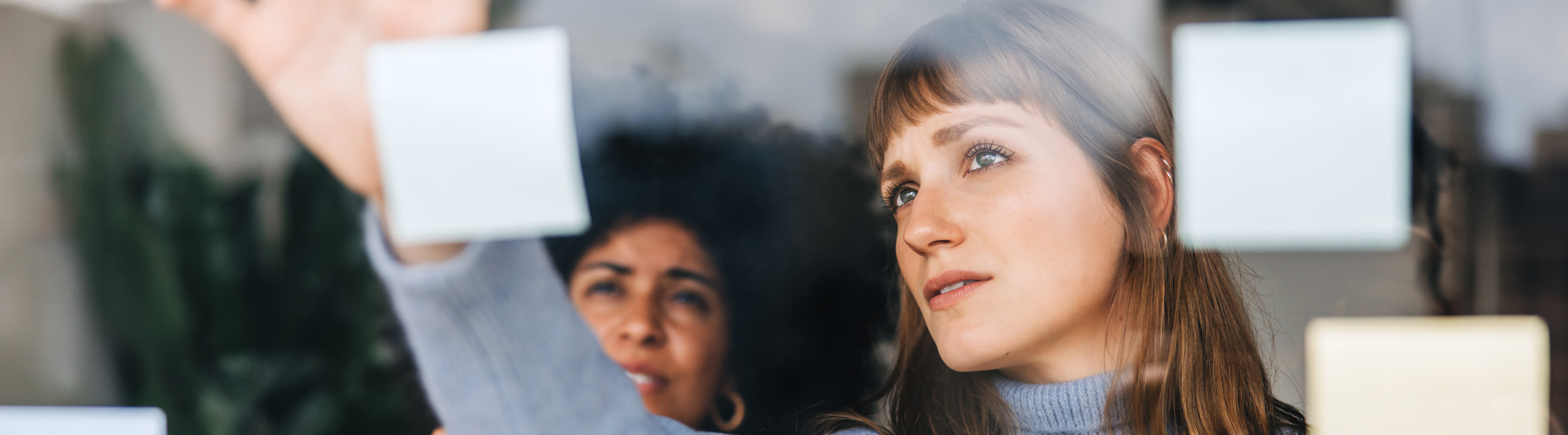 Two women placing sticky notes on a glass wall.