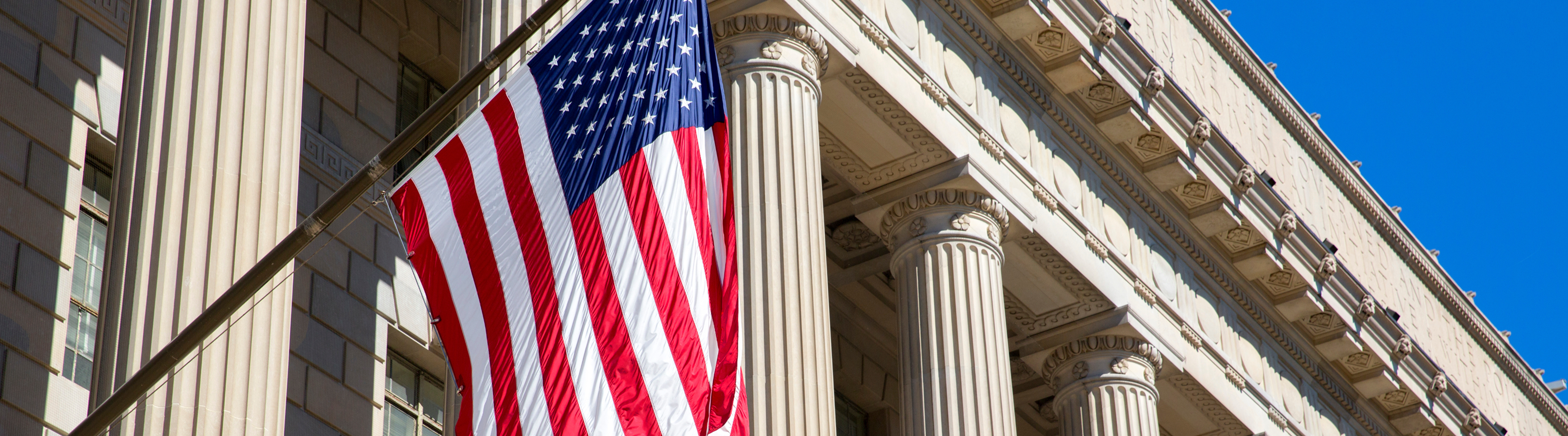 US flag waving in front of a neoclassical building with large columns.