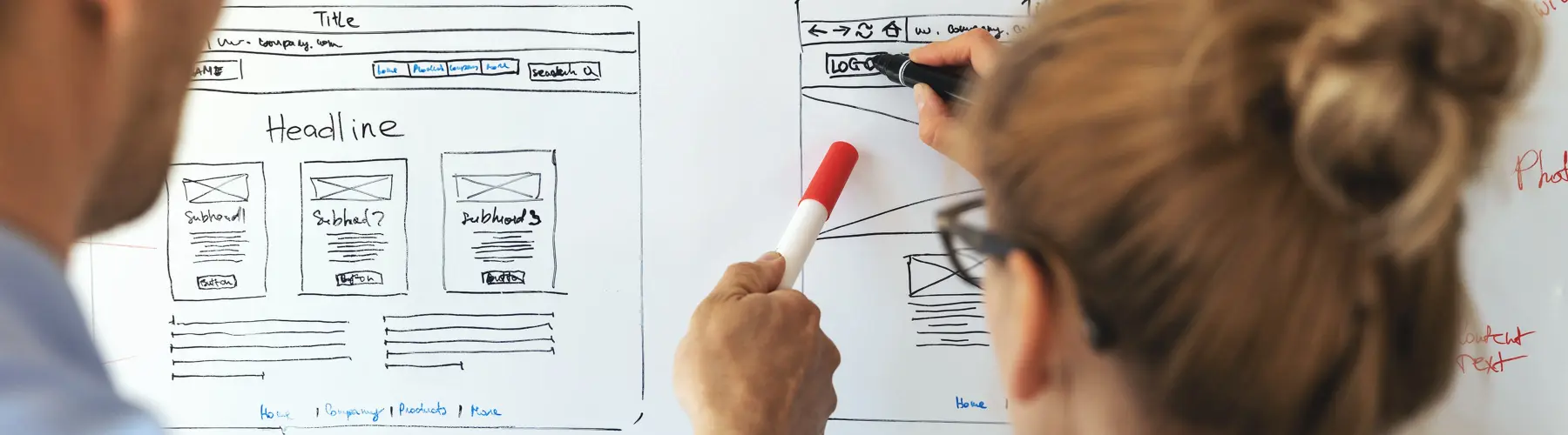 Two people discussing website sketches on a whiteboard.