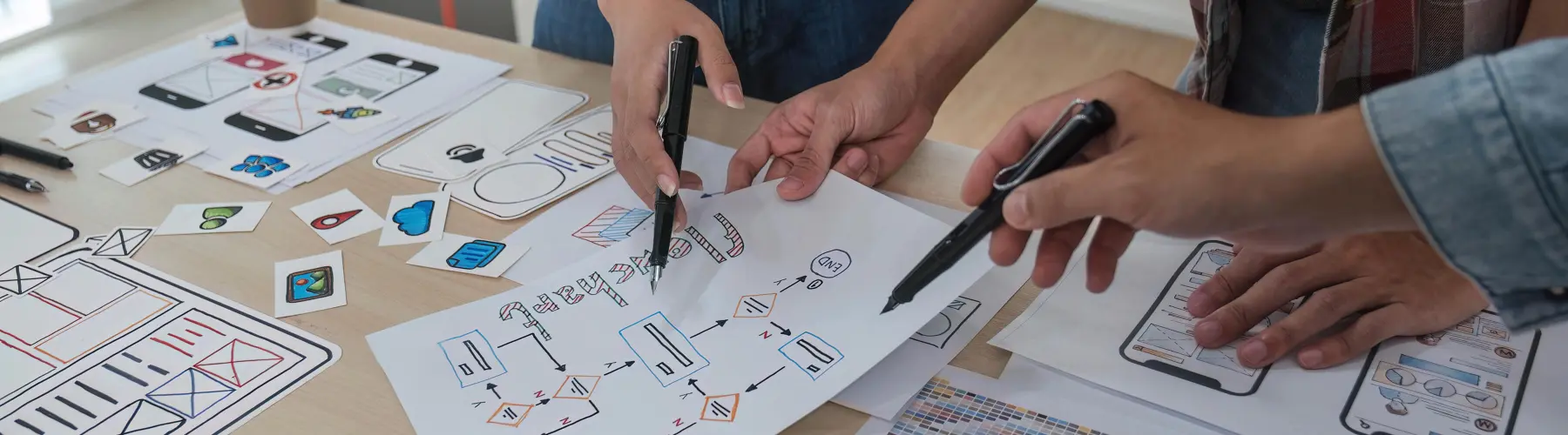 Hands collaborate on sketches and diagrams on a wooden desk.