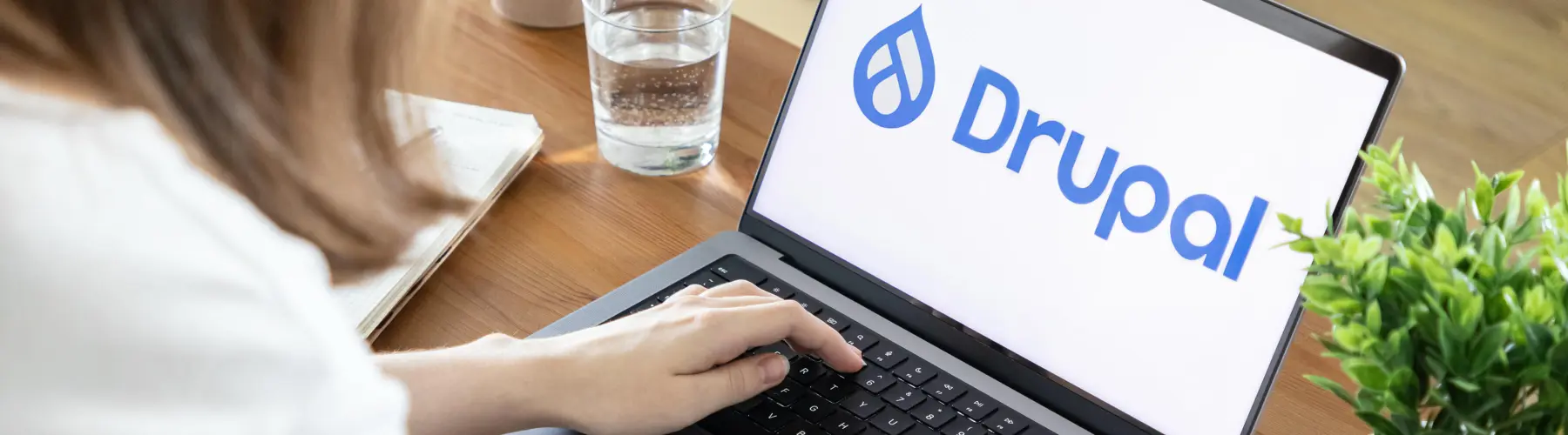 Person typing on a laptop with a Drupal logo on screen.