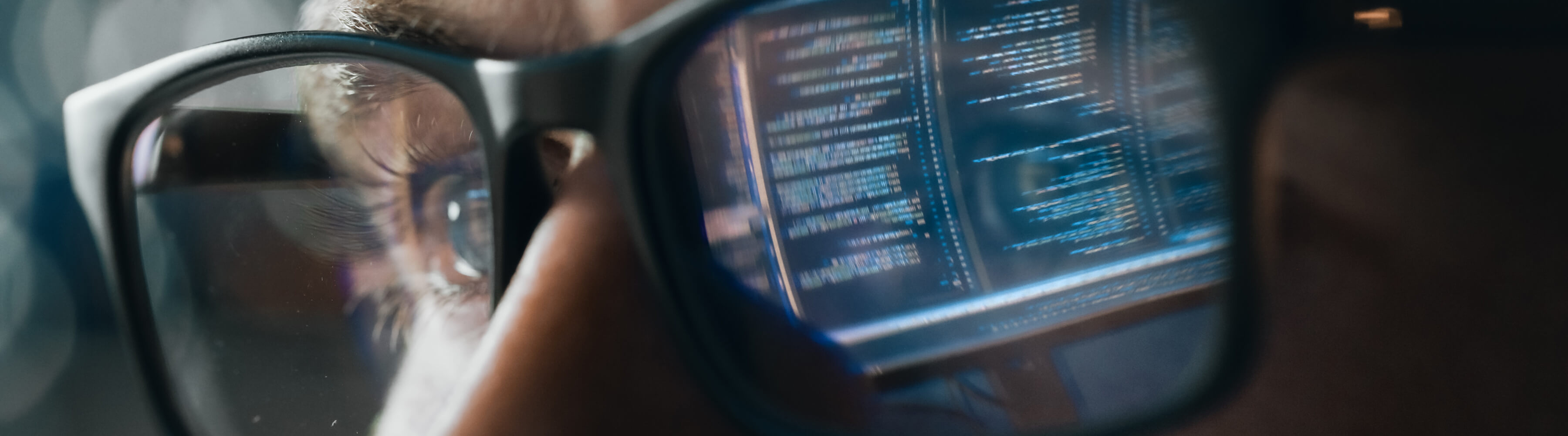 Close-up of glasses reflecting computer code, with a focused expression.