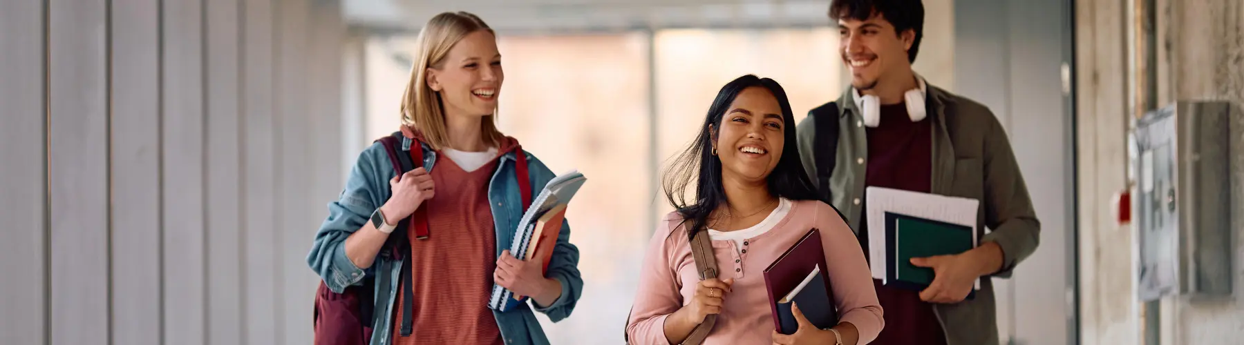 Three students walking in a hallway, smiling and carrying books.