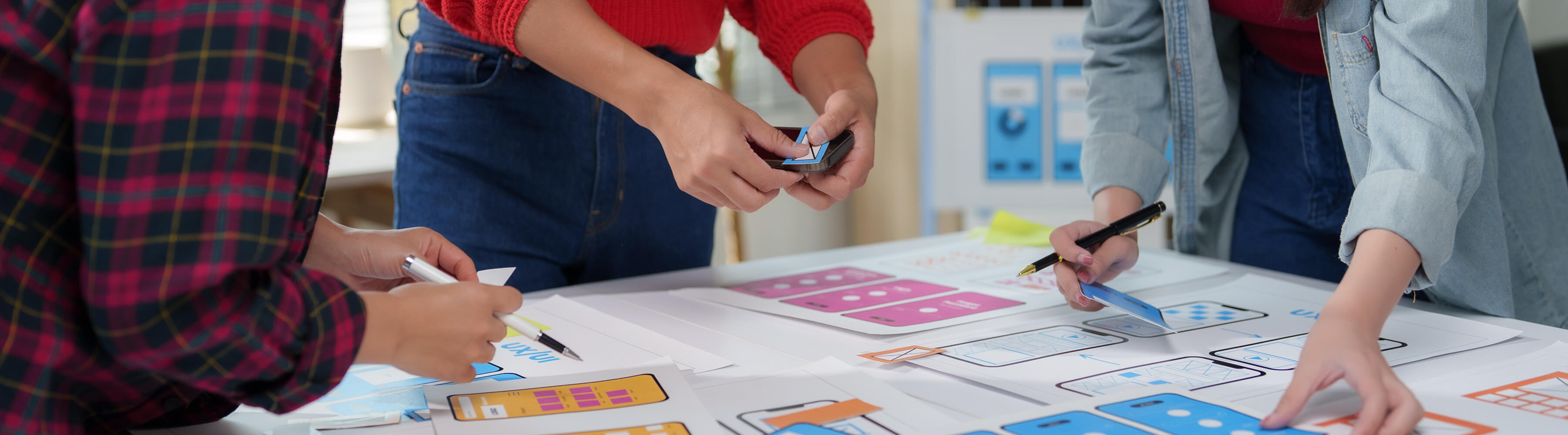 Designers working on colorful UX sketches and wireframes on a table.