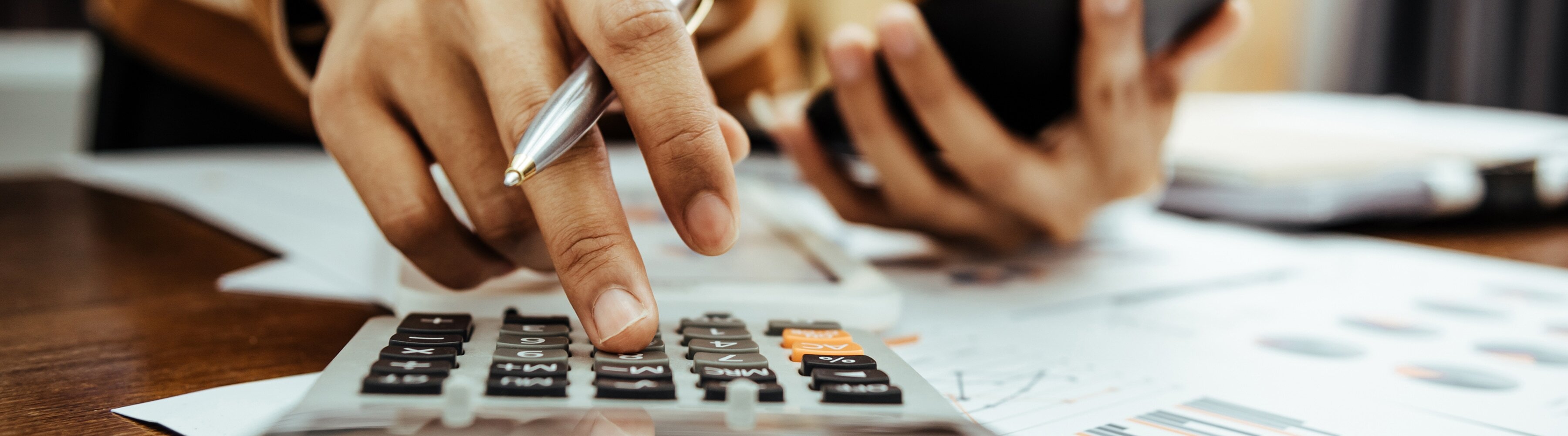 Hands using a calculator and holding a phone over paperwork.