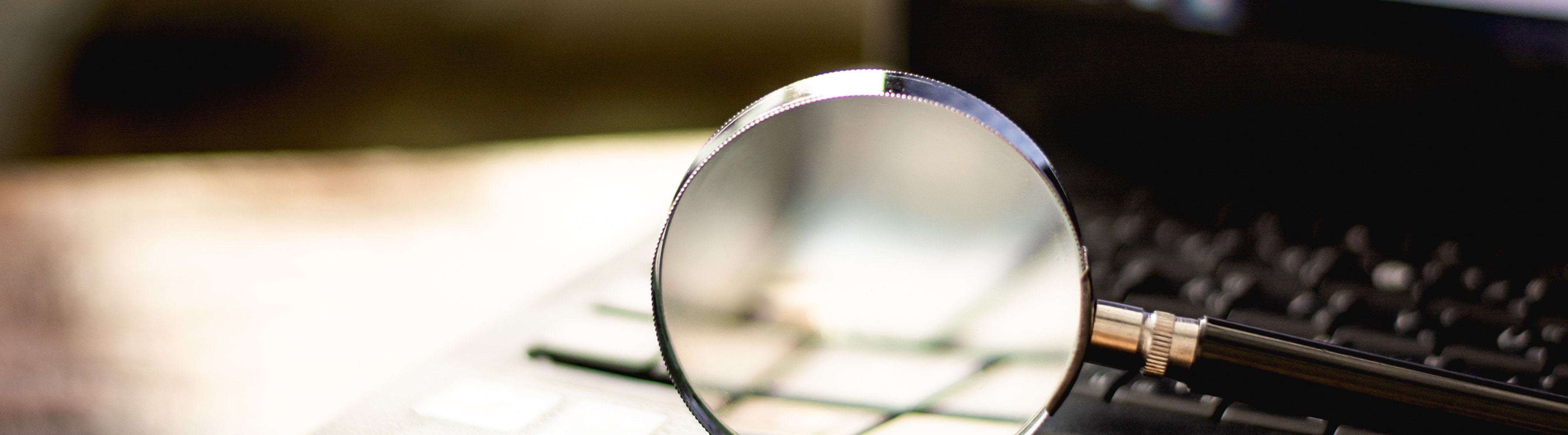 Magnifying glass on a laptop keyboard, softly lit background.