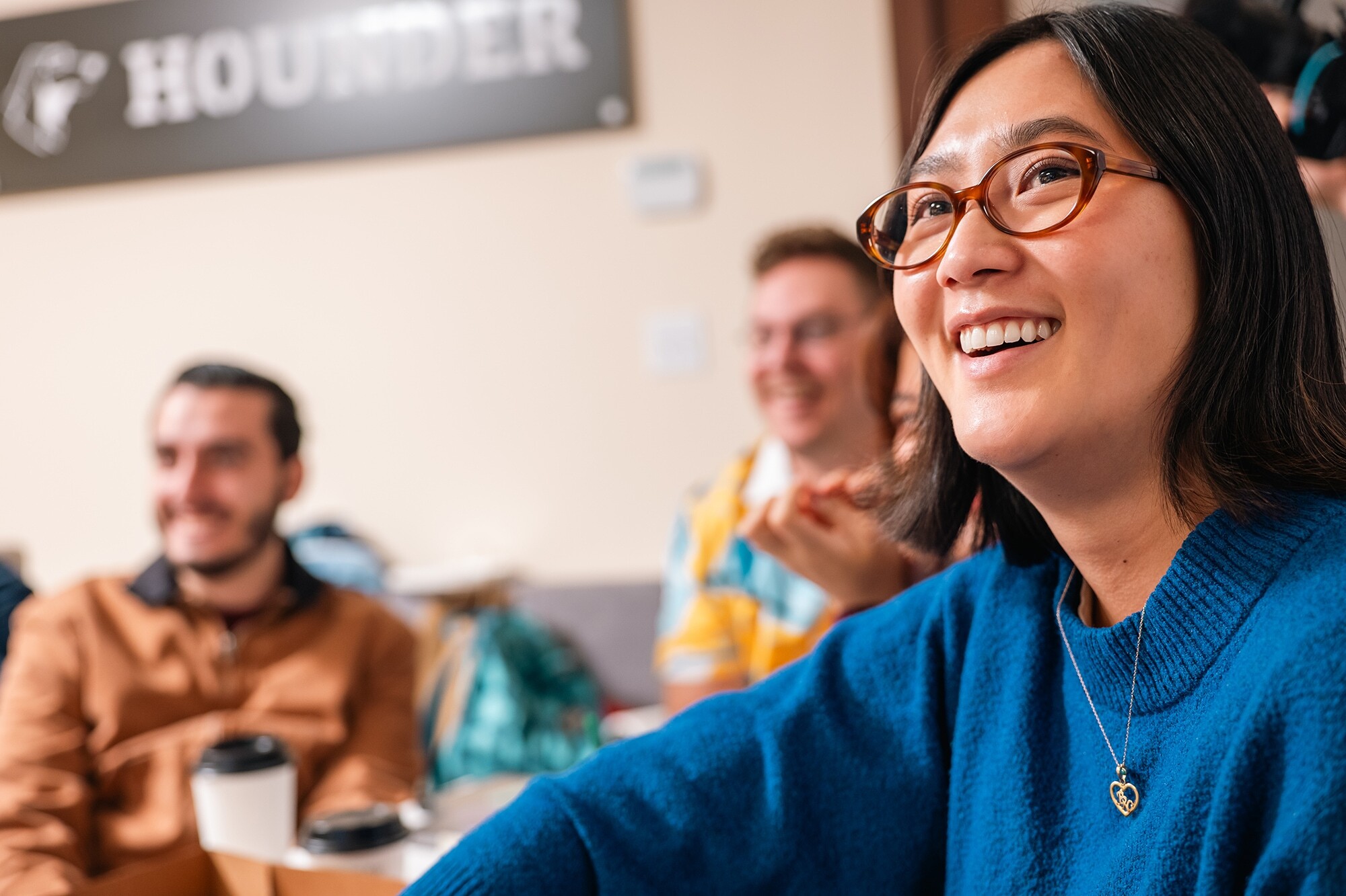 Smiling woman in blue sweater, sitting with friends in a cozy room.