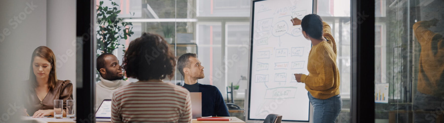 Team engaged in a presentation as a person points to a whiteboard.