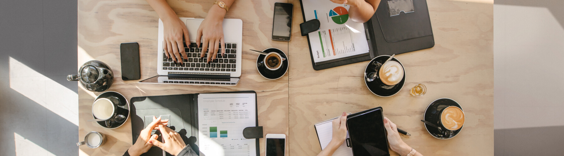 Overhead view of a business meeting with laptops, documents, and coffee on a wooden table.