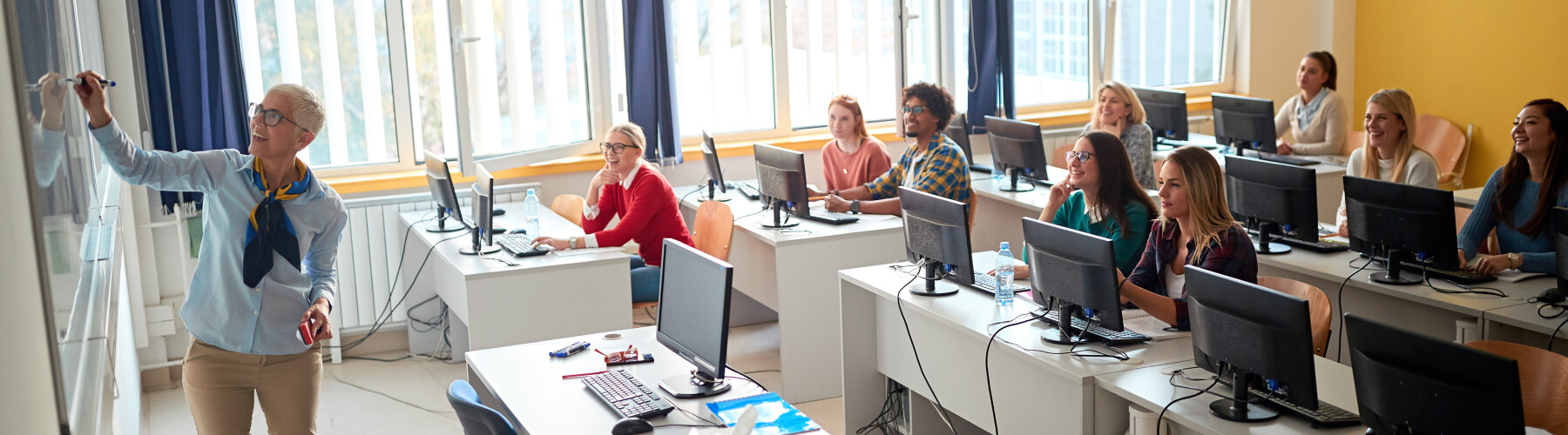 Teacher instructing attentive students in a computer classroom.