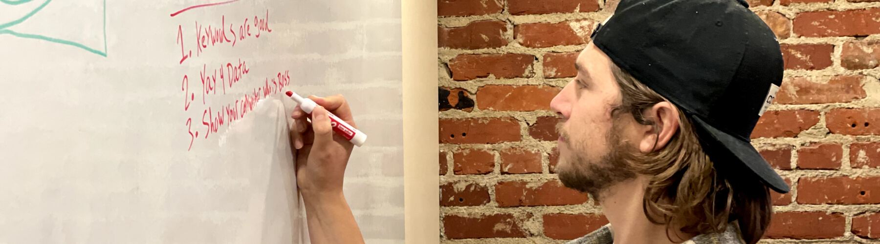 Person writing notes on a whiteboard with a red marker.