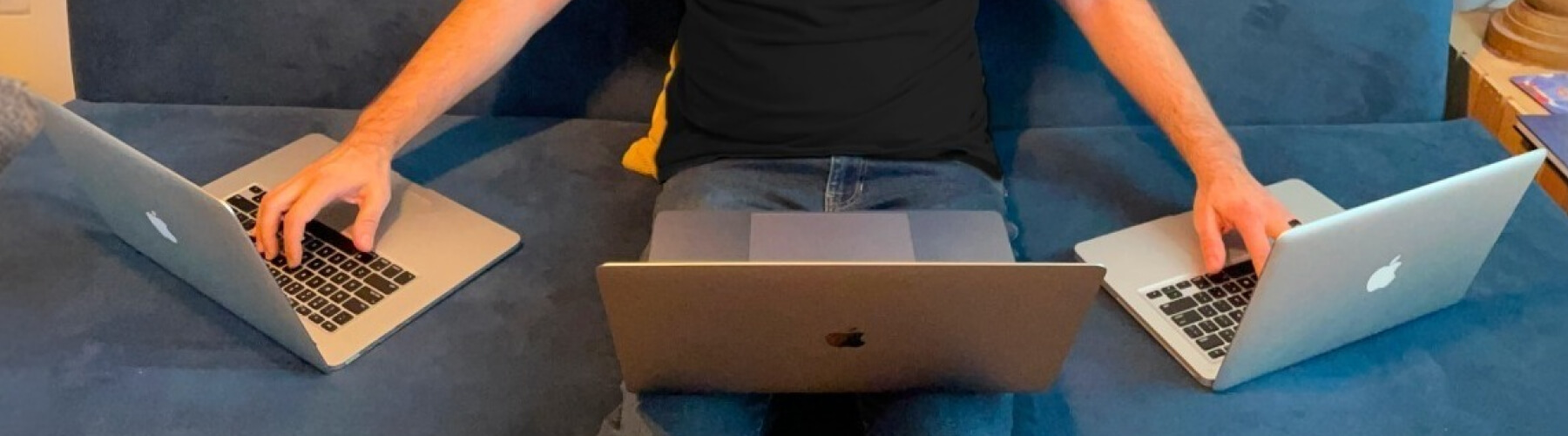 Person multitasking with three laptops on a sofa.