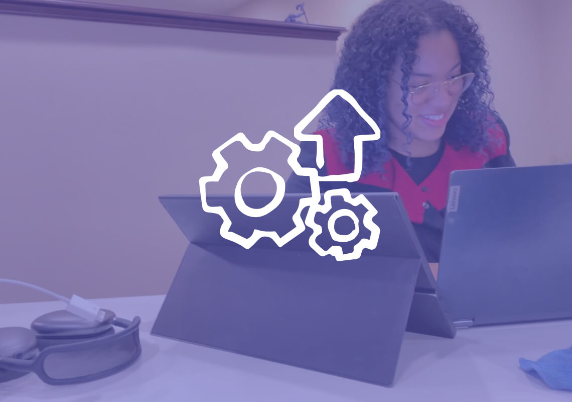 Smiling woman working on two laptops at a desk.