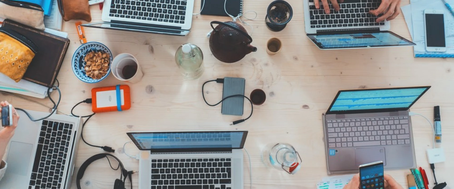 Overhead view of teamwork with laptops and gadgets on a wooden desk.