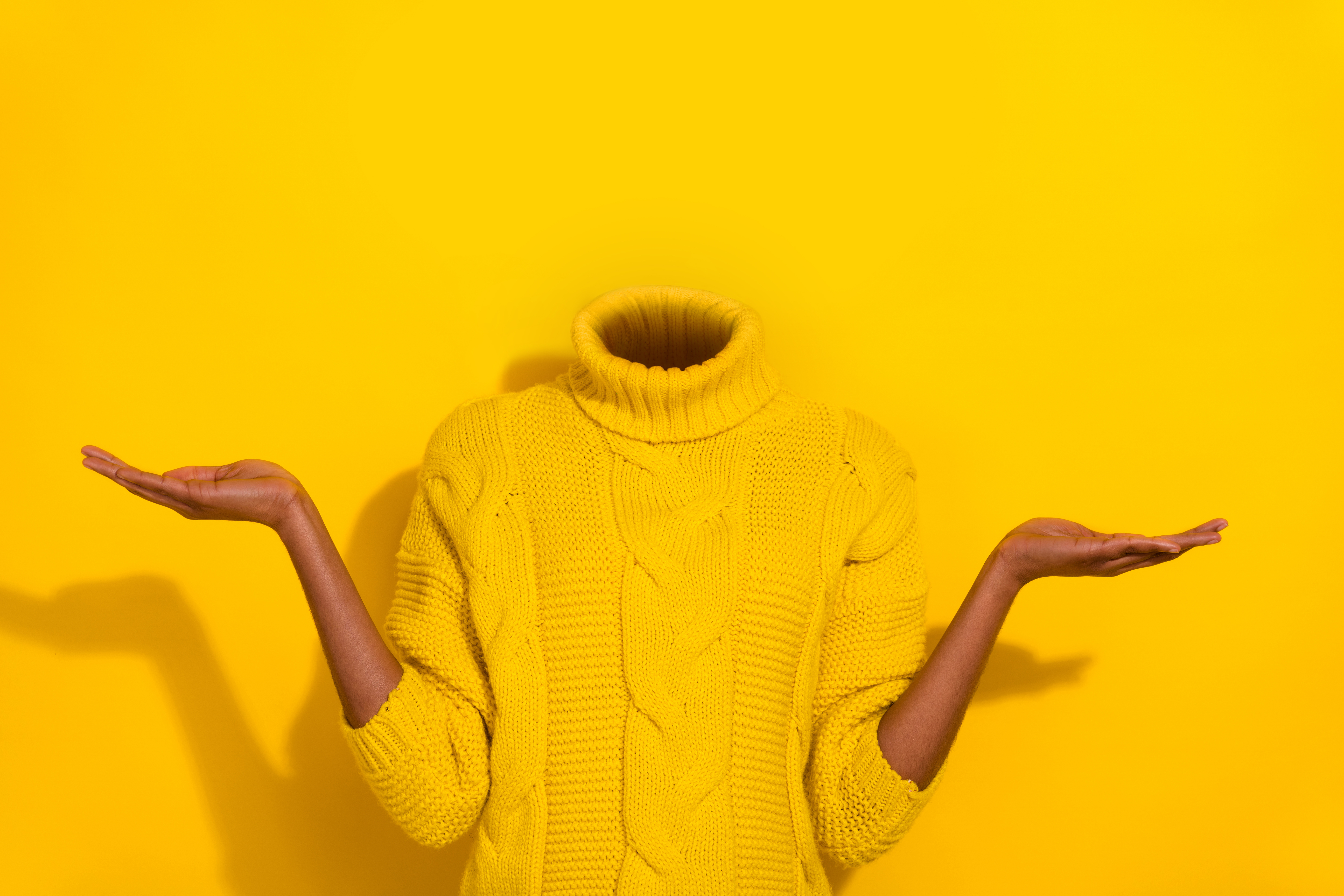 Headless person in a yellow sweater shrugging on a matching yellow background.