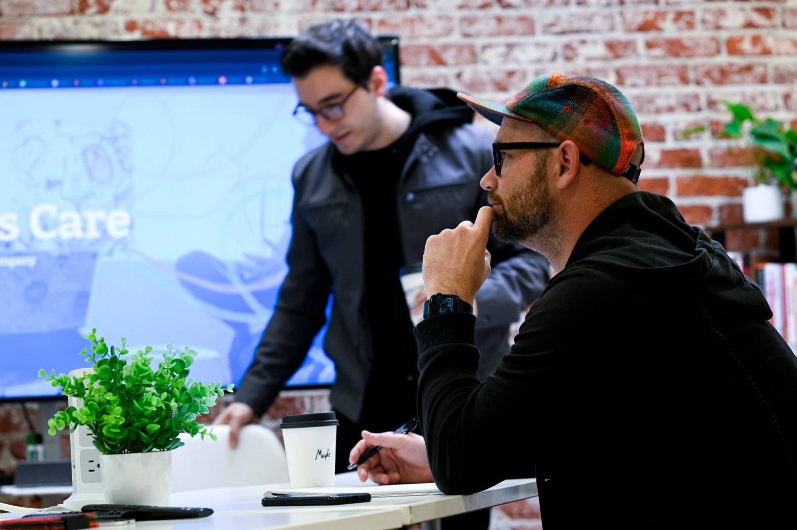 Two men in casual office setting with a presentation background.