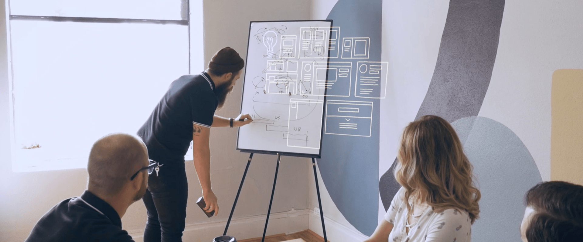 Team brainstorming session with a man sketching on a whiteboard.