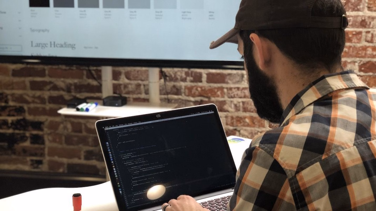 Developer coding on a laptop with a design board in the background.