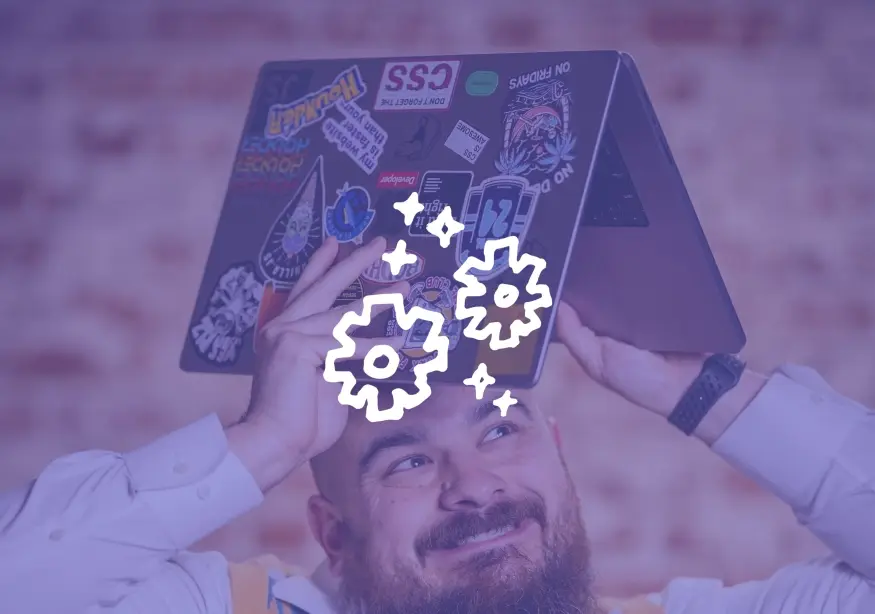 Man joyfully holds a sticker-covered laptop over his head with gear icons.