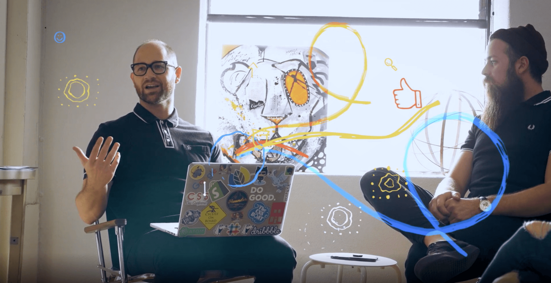 Two men in a discussion with a laptop, colorful abstract lines overlaid.