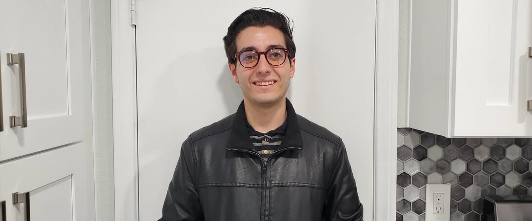 Smiling person wearing glasses and a black leather jacket in a kitchen setting.