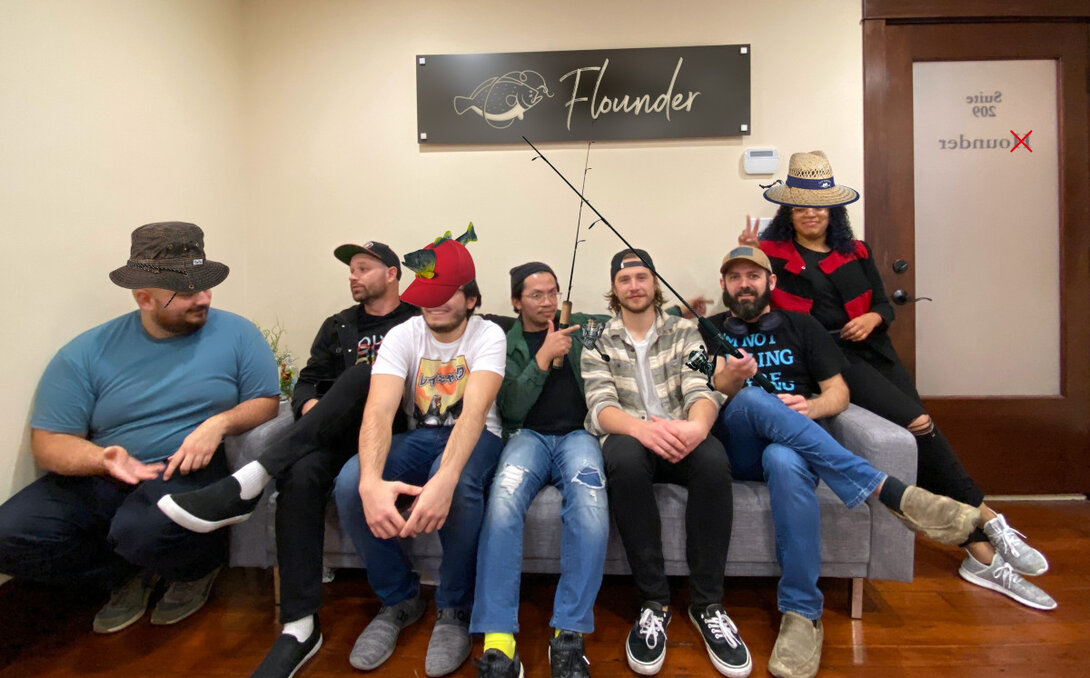 Group of people wearing hats with fishing theme under "Flounder" sign on a couch.