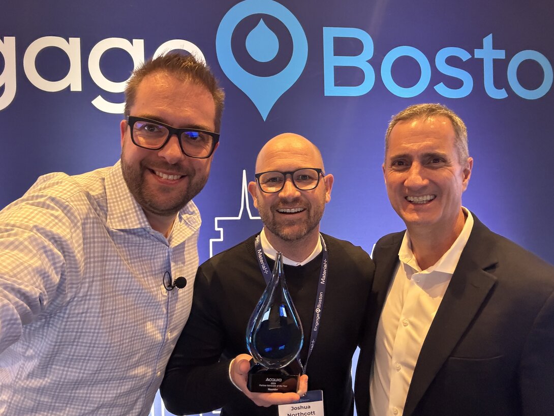 Three men smiling at a conference, one holding an award, "Boston" sign in the background.