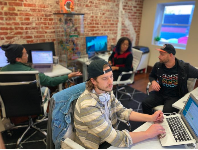 Diverse team collaborating in an exposed brick office with laptops and monitors.