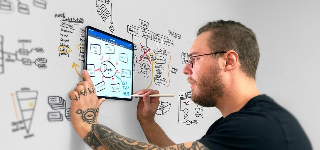 Man using a tablet and stylus to brainstorm digital concepts on a whiteboard.