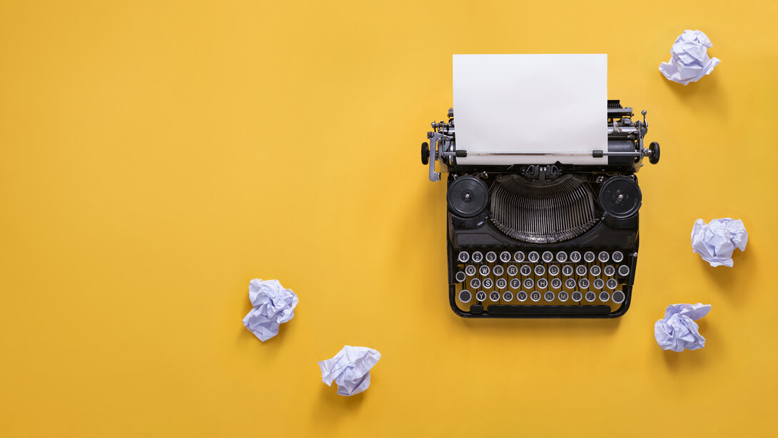 Vintage typewriter with crumpled paper on yellow background.
